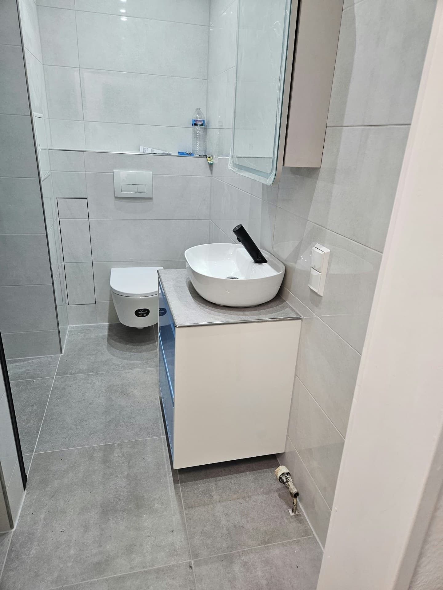 Bad mit hellgrauen Wand- und Bodenfliesen, Waschtisch mit Aufsatzbecken und Wand-WC